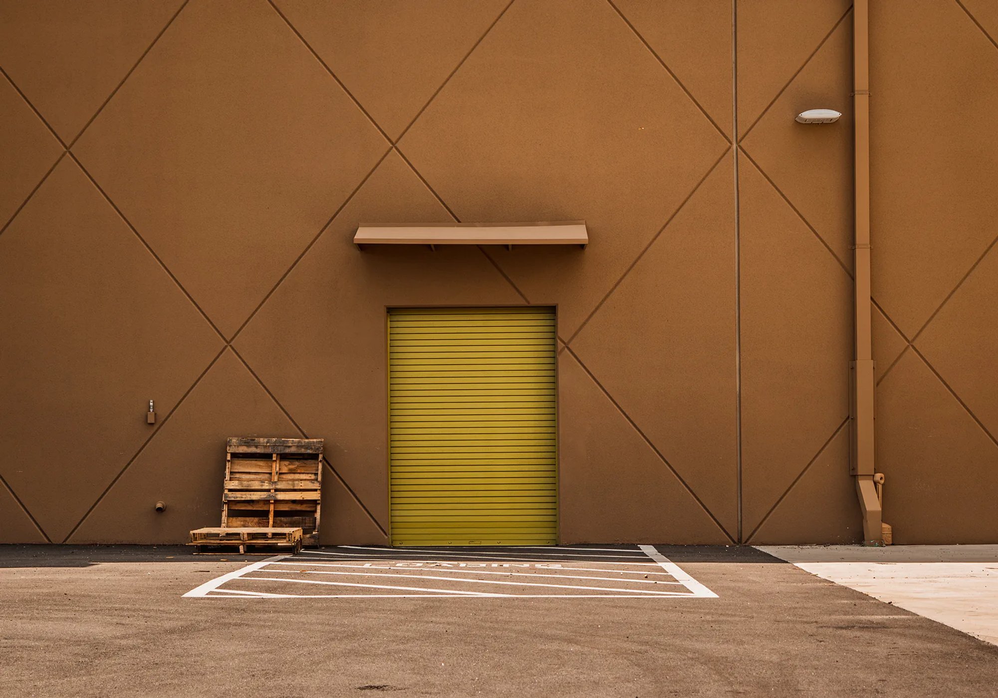 Brown warehouse wall with a green roll-up door and stacked pallets.