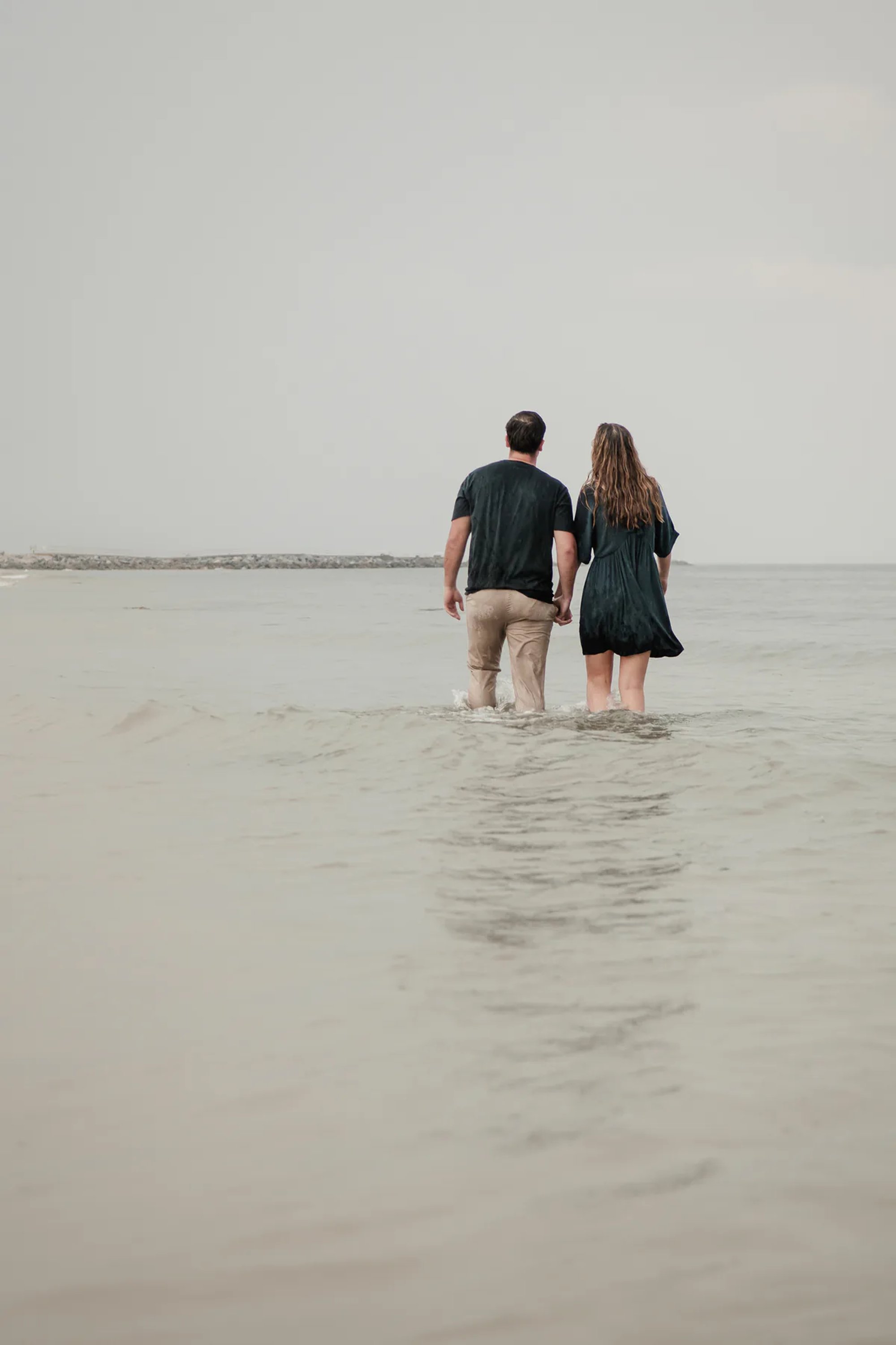 Couple standing in shallow water during Ponce Inlet engagement photos on a rainy beach