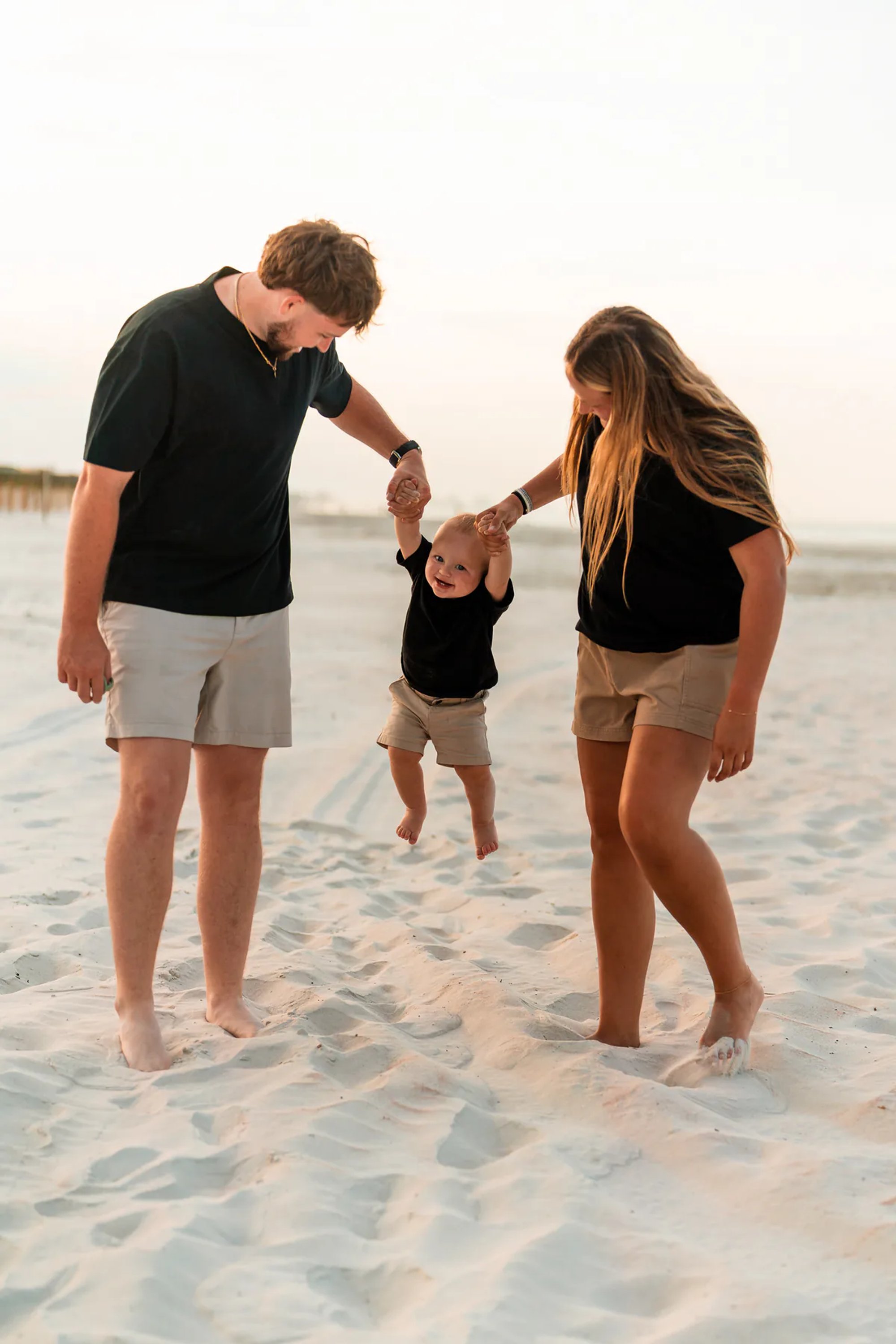 Parents holding their child’s hands while walking through the sand at Ponce Inlet Jetty Beach.