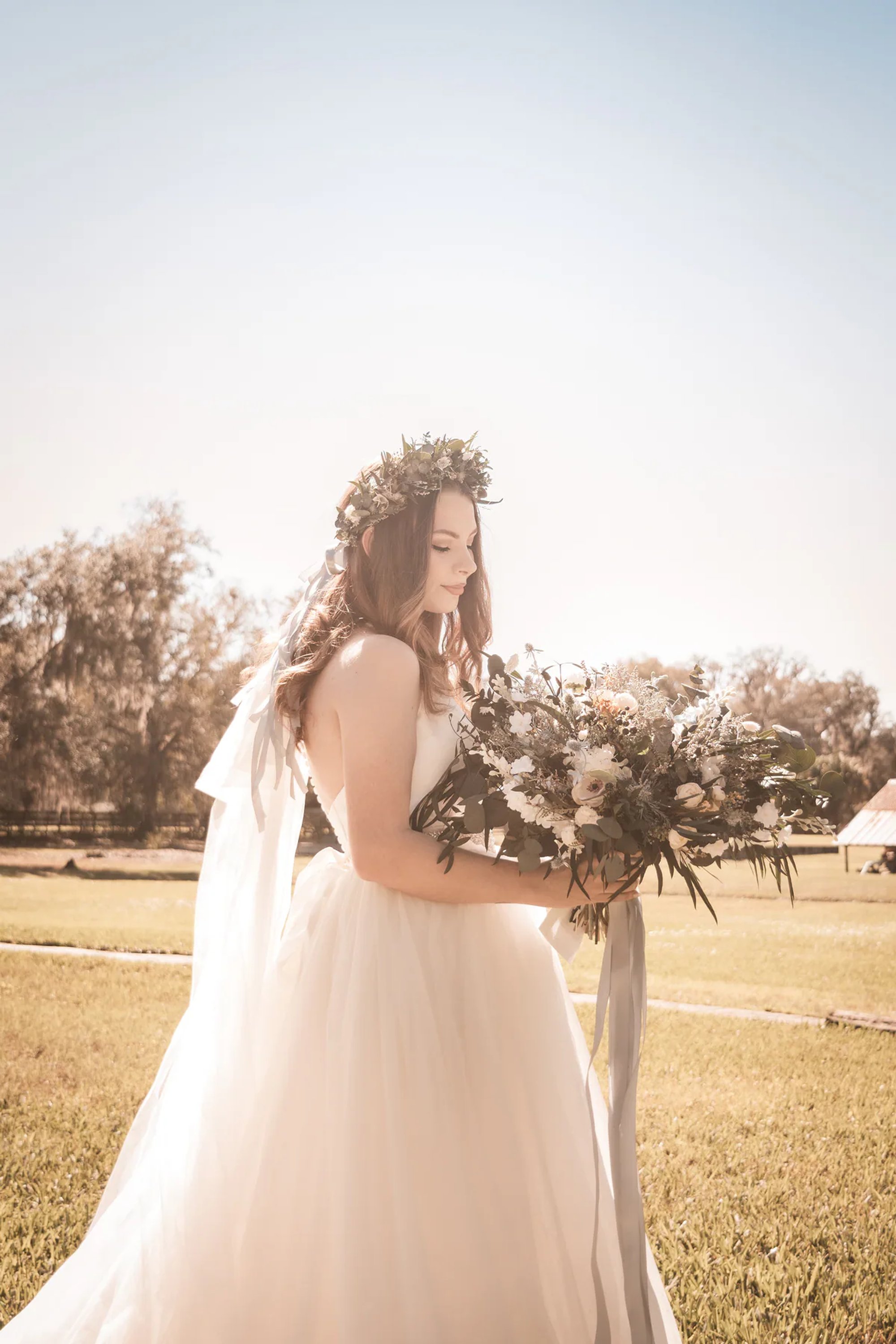 Bride holding her bouquet in warm backlight on an open lawn.