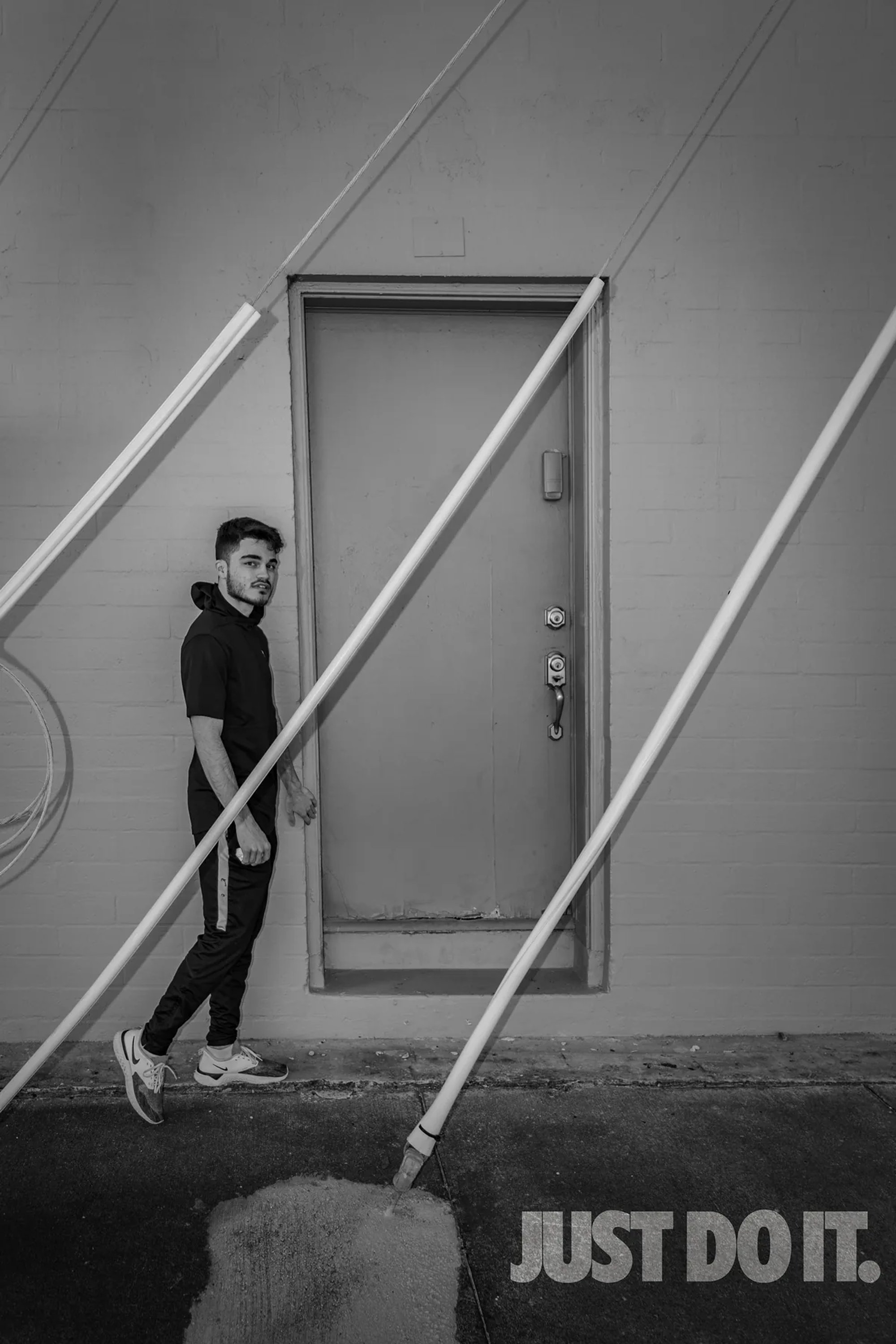 Black-and-white portrait of a man on metal stairs beside an industrial door.