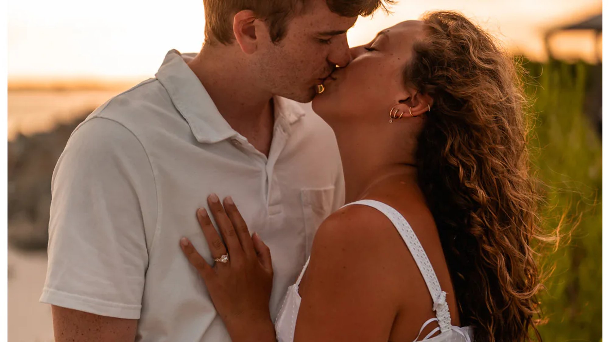Couple kissing in warm sunset light near the beach.