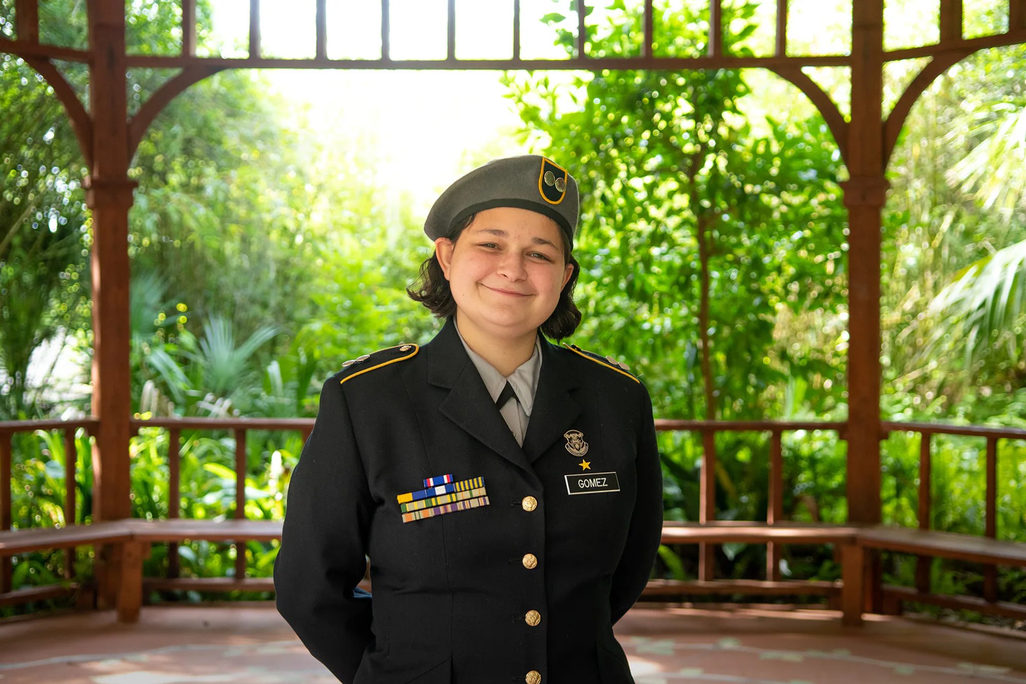 Young person wearing a decorated military-style dress uniform in a leafy gazebo.
