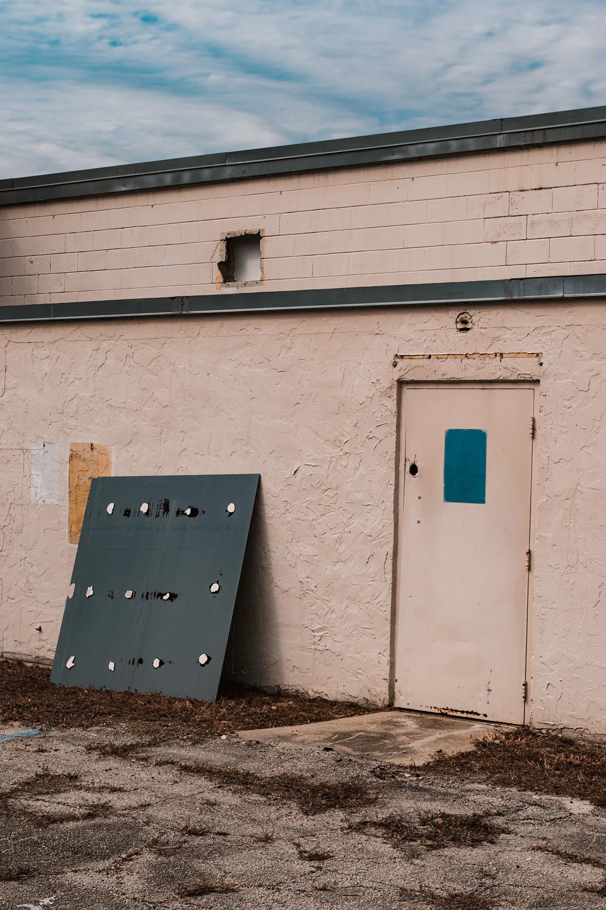 Pale industrial wall with a teal door and detached metal panel.