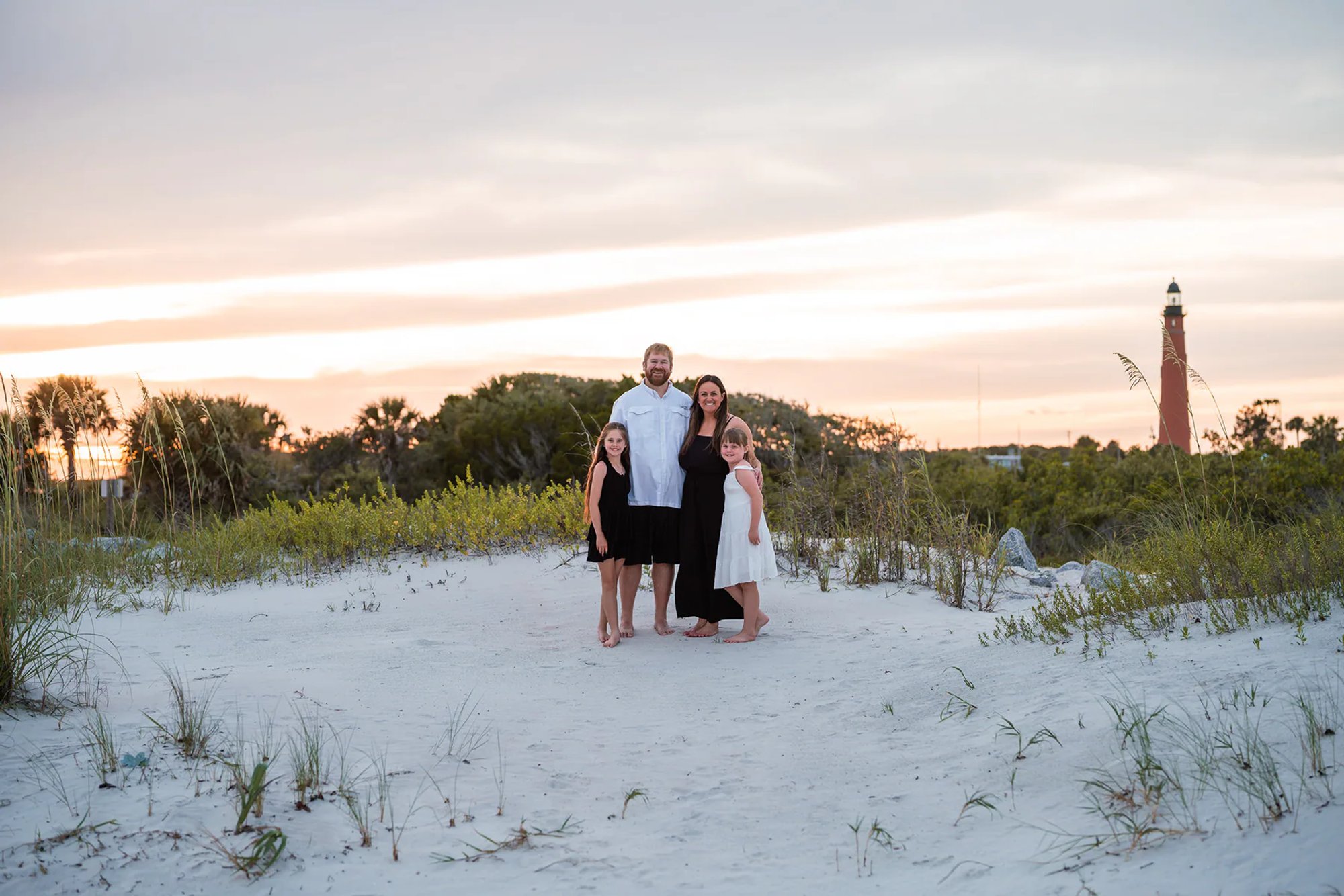 Family standing in the dunes near Ponce Inlet Lighthouse during a beach photo session.