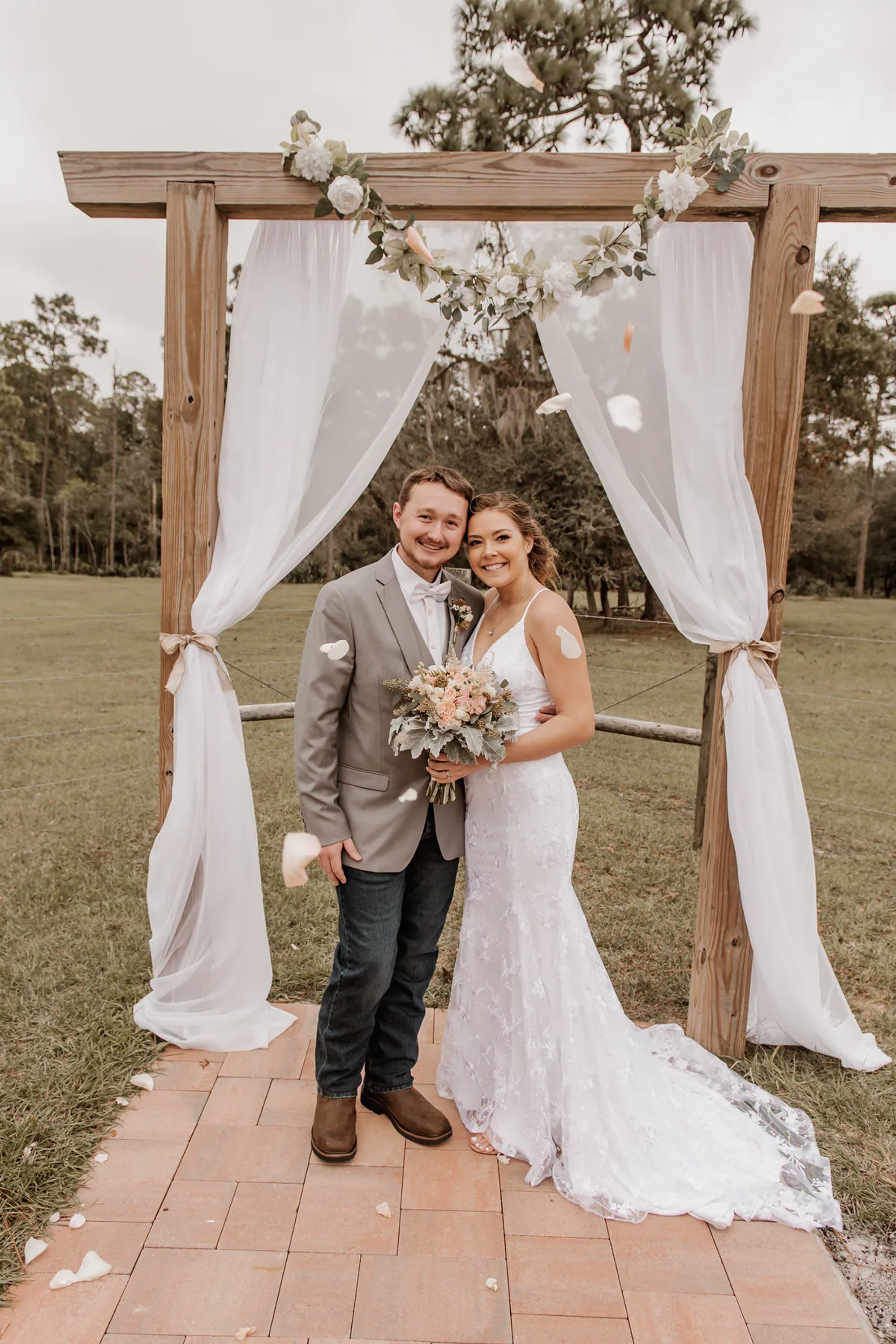 Bride and groom beneath a wooden wedding arch draped in white fabric.