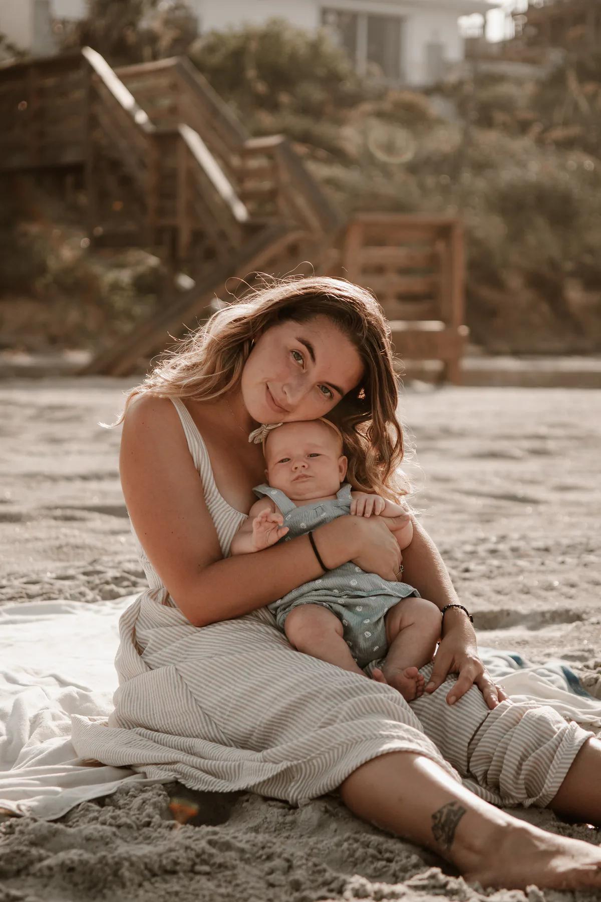 Mother cuddling her baby while seated on the beach.