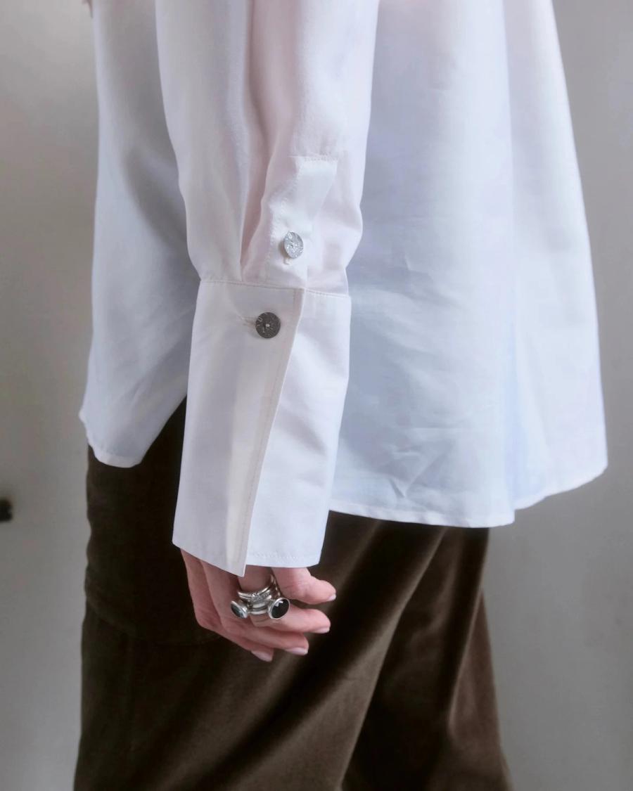 Close up detail of a shirt cuff developed for independent sustainable womenswear brand Studio Wylder based in East London. The shirt features a distinctive, exaggerated cuff architecture with delicate mother of pearl buttons, showcasing its considered construction and refined detailing. Studio Iole worked as the freelance pattern cutter, developing the creative pattern through fittings and refinements and working closely on the cuff construction through to the final sealed production pattern used to produce the finished garment shown. The image also highlights the premium finish of the double turned split side dolphin hem.