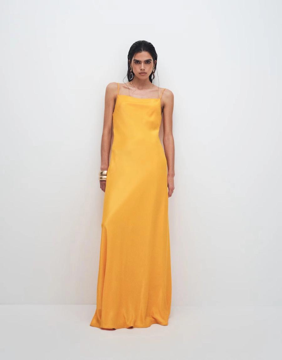 Model wearing the Viscose Satin Low Scoop Maxi Slip Dress by Topshop. The glossy orange satin-style dress has a clean, fluid maxi silhouette with a regular fit and is cut on the bias, allowing the fabric to fall naturally around the body. The front features a square neckline finished with delicate rouleau straps, while the back has a low scoop shape that follows the fluid line of the dress. A clean finish has been achieved by bagging out the neckline with self lining and edge stitching the finish. The simple construction allows the colour, fabric and bias cut to create the main visual impact. Iole developed the pattern as the creative pattern cutter, working through the bias cut, fit, neckline, straps and back shape to achieve a clean finish.