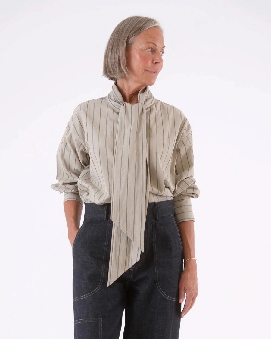 Model wearing the Edie Bow Shirt in a studio setting for a commercial garment shoot. The shirt features a slightly oversized, relaxed fit with dropped shoulders for a considered, loose tailored silhouette. A bespoke stand collar extends into a dramatic front tie, which can be worn as a bow or styled over the shoulder for a more contemporary look. Studio Iole developed the creative pattern through fittings and refinements, working closely on the fit, silhouette and construction through to the final sealed production pattern used to produce the finished garment shown.