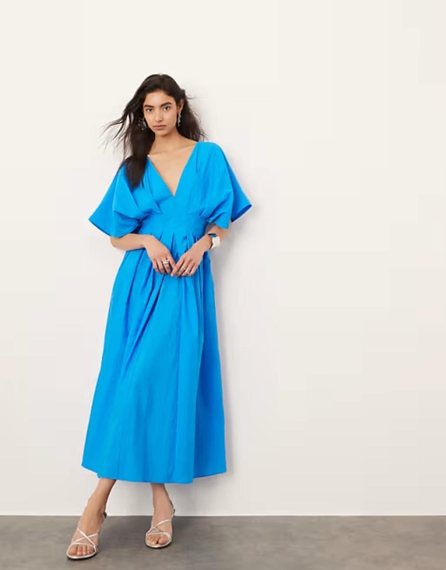 Model wearing a blue structured midi dress from ARRANGE, photographed in a professional studio setting for ASOS.com. The dress features a clean V-neckline, short sleeves, fitted bodice and defined waist, flowing into a softly structured midi-length skirt. The silhouette is fitted through the upper body before gently releasing through the skirt, highlighting the considered shaping and clean lines of the garment.