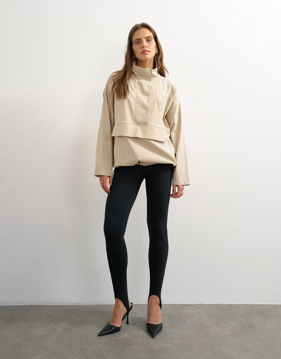 Model wearing the Technical Funnel Neck Jersey Track Top by Topshop in a stylised fashion shoot. The stone grey jacket is shown as a full front view highlighting the structured funnel neck, concealed front placket and relaxed shape. The model wears oversized black ski-inspired sunglasses, adding a bold fashion-led styling element to the contemporary sportswear-inspired design. The funnel neck is the main focus of the image, showing the shape and construction of the collar in detail. Iole worked as the creative pattern cutter, developing the jacket pattern and refining the proportions and construction of the funnel neck, placket and overall silhouette.