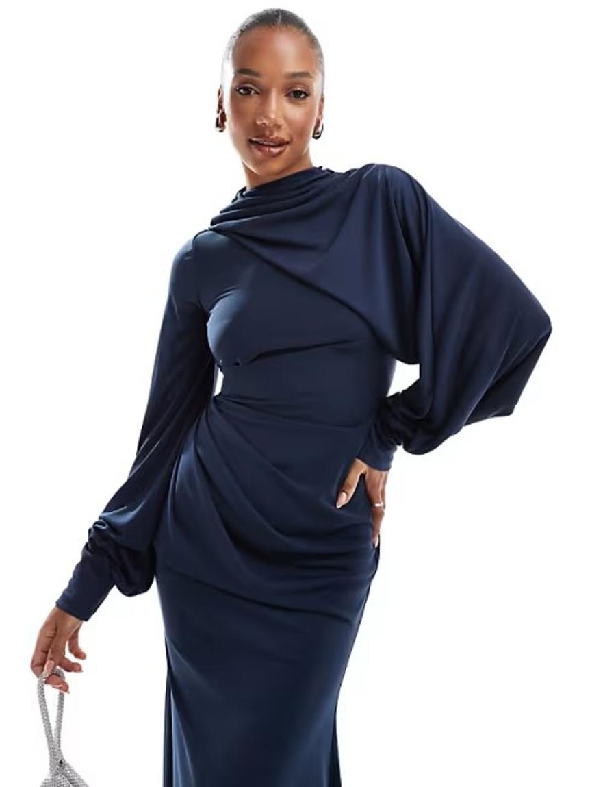 A model wears a dark blue, floor-length jersey maxi dress in a studio against a crisp white background. The dress features a high draped neckline with softly gathered fabric through the bodice, subtle gathering at the fitted waist, and long voluminous blouson sleeves gathered at the wrists. The fluid silhouette falls to the floor, creating a modest full length shape. The garment was draped on the stand before being digitised into Vetigraph, a CAD digital pattern cutting software.