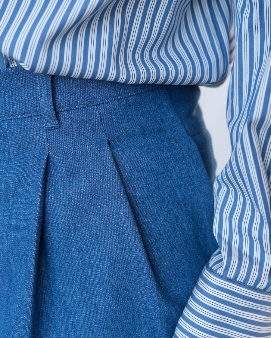 Detail view of the Shiloh Trouser by independent sustainable womenswear brand Studio Wylder, focusing on the double pleated front and waistband construction. The relaxed trouser features a carefully shaped waistband, double pleats and considered stitching details, with the organic denim highlighting the structure of the garment. Iole worked as the creative pattern cutter, developing and refining the pattern through fittings before grading the pattern in her East London studio into additional sizes to create a more size-inclusive fit. The final production pattern was prepared for manufacture.