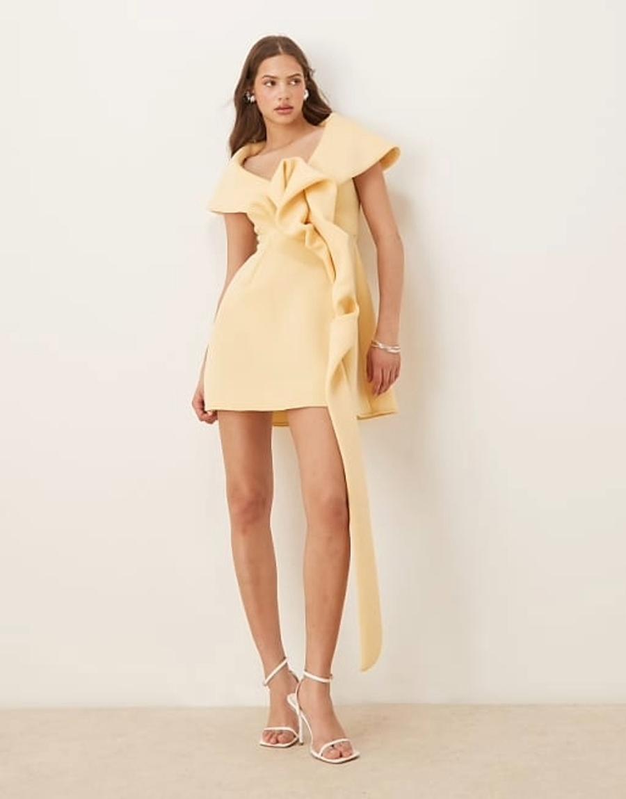 Model wearing the off shoulder mini dress with manipulated front detailing by ASOS Design, photographed in a studio setting. The buttermilk dress is made from a structured scuba-style fabric and features an off shoulder neckline, fitted bodice and clean A-line mini skirt. The front bodice has sculptural manipulated fabric detailing, creating folds and shaping across the bust and waist. The structured fabric helps to hold the defined shape of the bodice and clean lines of the skirt. Iole developed the pattern as the creative pattern cutter, working through the off shoulder neckline, manipulated front detailing, fit and proportions of the dress.