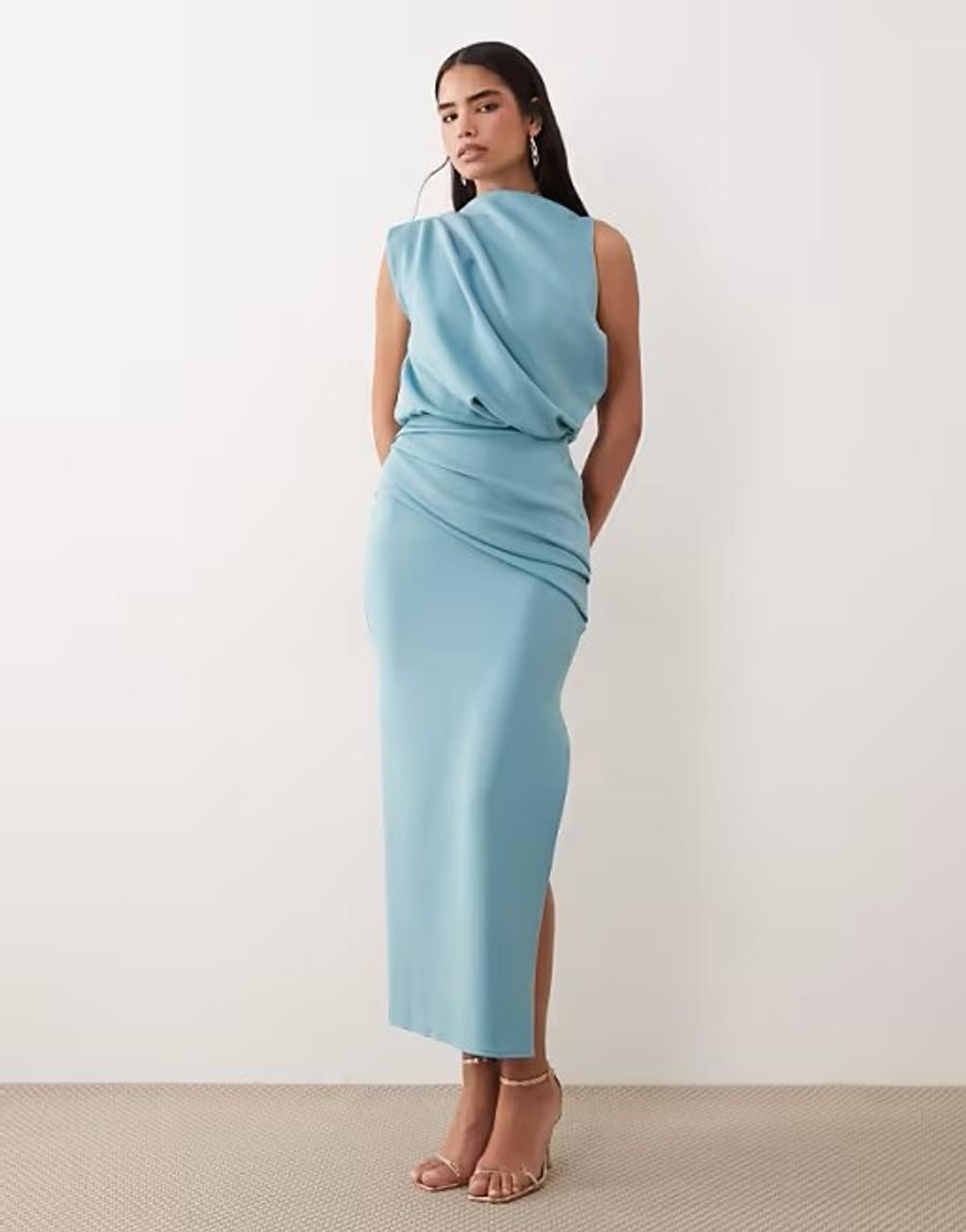 Model wearing the draped structured midi dress with split in blue by ASOS Design, photographed against a plain off-white studio background. The light blue sleeveless dress features a draped blouson-style bodice with asymmetric pleated detailing through the hip, creating soft volume and movement across the body. The fitted midi skirt follows the figure and is finished with a side split, balancing the fluid draping of the bodice with a clean, elongated silhouette. The model wears gold ankle-strap high-heeled sandals, with her long dark hair styled straight and parted down the middle. Iole developed the pattern as the creative pattern cutter, working through the fit, proportions, draped bodice and asymmetric pleated hip detail. Digitally pattern cut using Vetigraph CAD Pattern cutting software. 