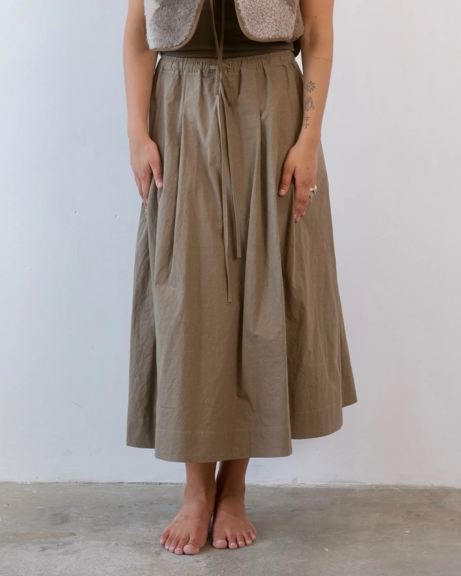 Model wearing the Suki Drawstring Skirt by independent sustainable womenswear brand Studio Wylder. Made from 100% organic washed Japanese cotton, the midi skirt has a softly shaped waist that opens into a full, fluid deep hem. The stitched down pleats with contrast topstitching are carefully positioned to create the volume and movement, while the drawstring waist allows the fit to be adjusted. Deep, discreet pockets are built into the side seams for a clean finish. Studio Iole worked as the creative pattern cutter, developing the fit and construction through fittings and refinements through to the final production pattern.