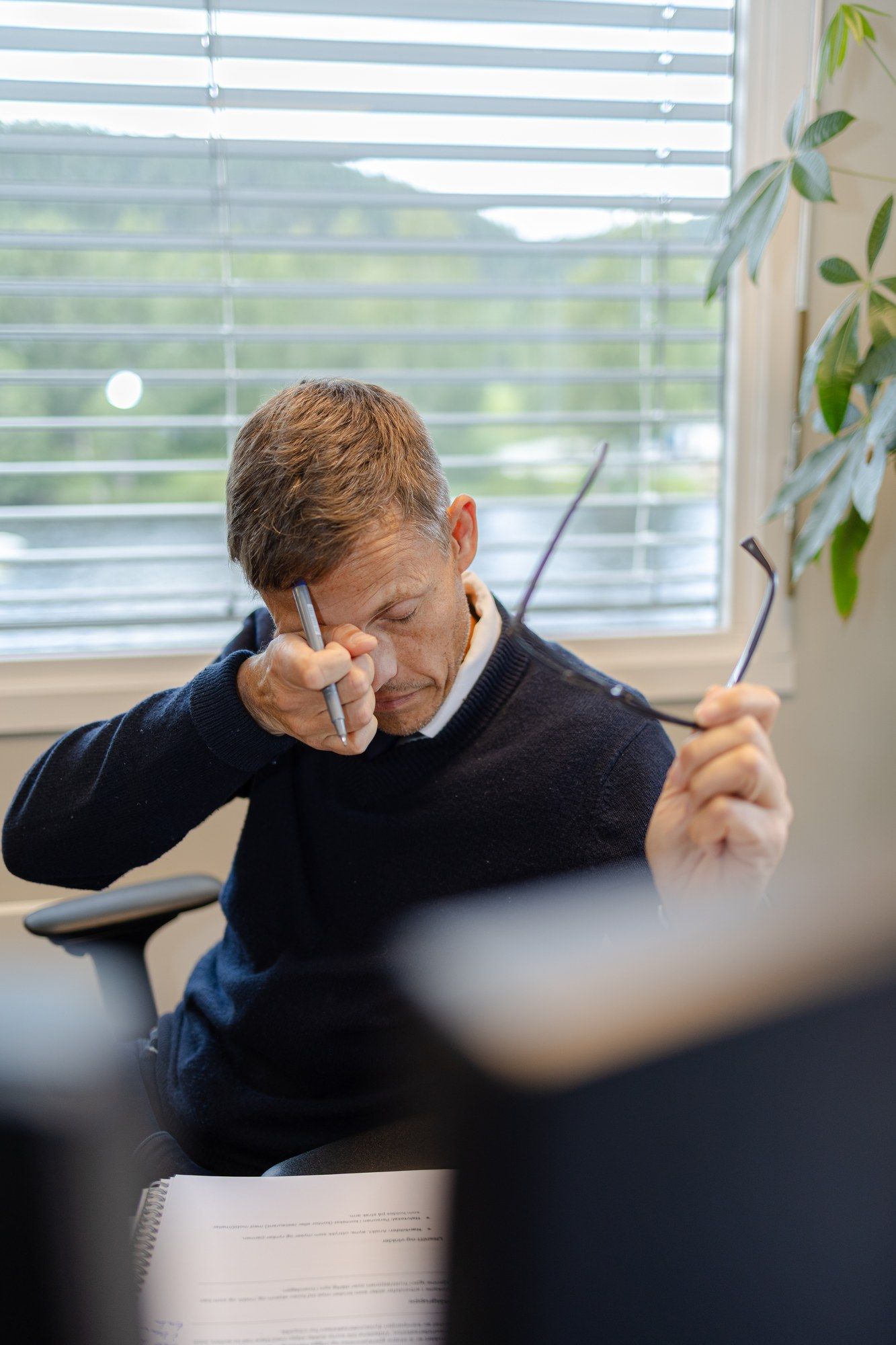 Mann med tørre og slitne øyne gnir seg i øynene ved arbeidsplassen