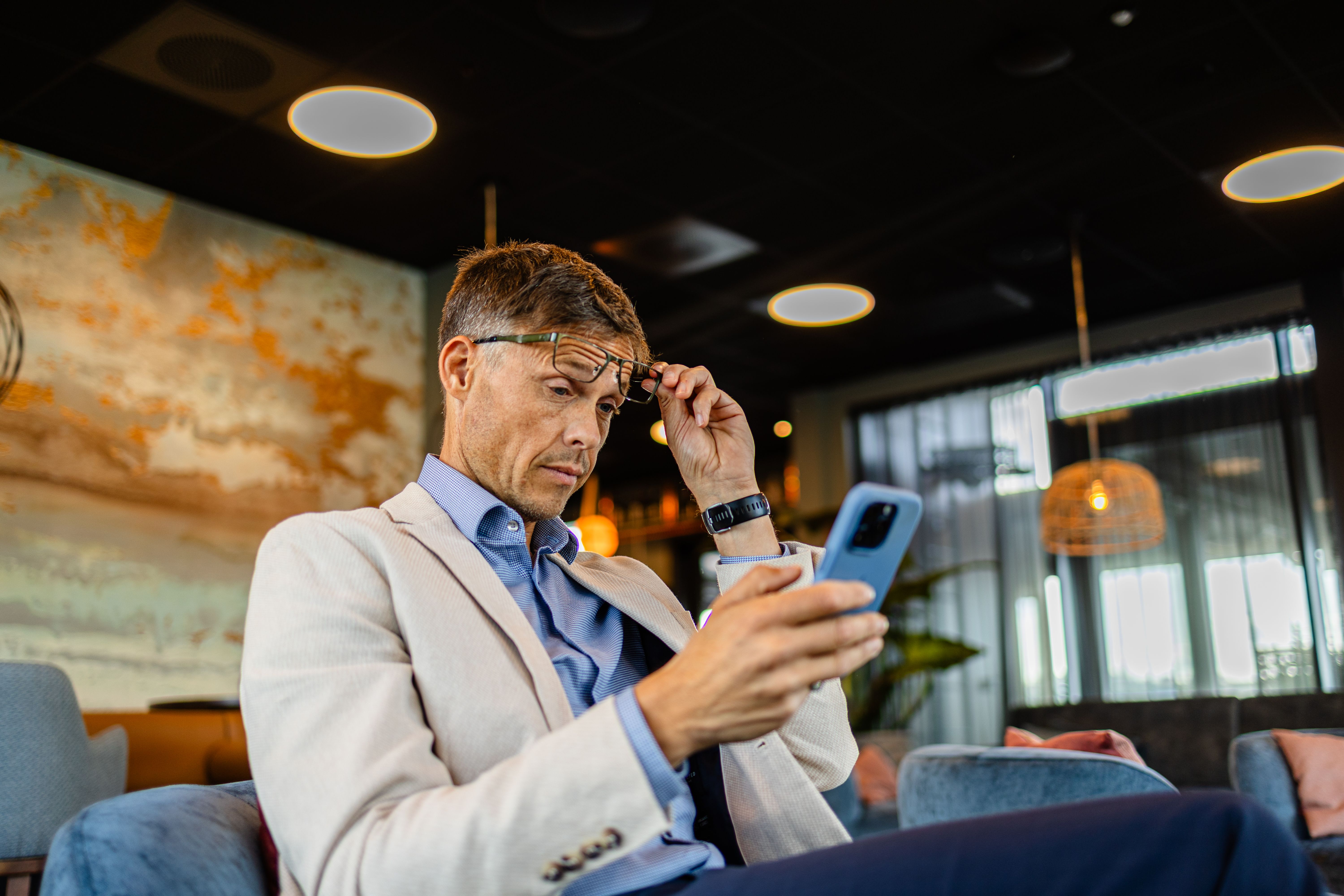 Mann løfter lesebrillene for å se på mobilen