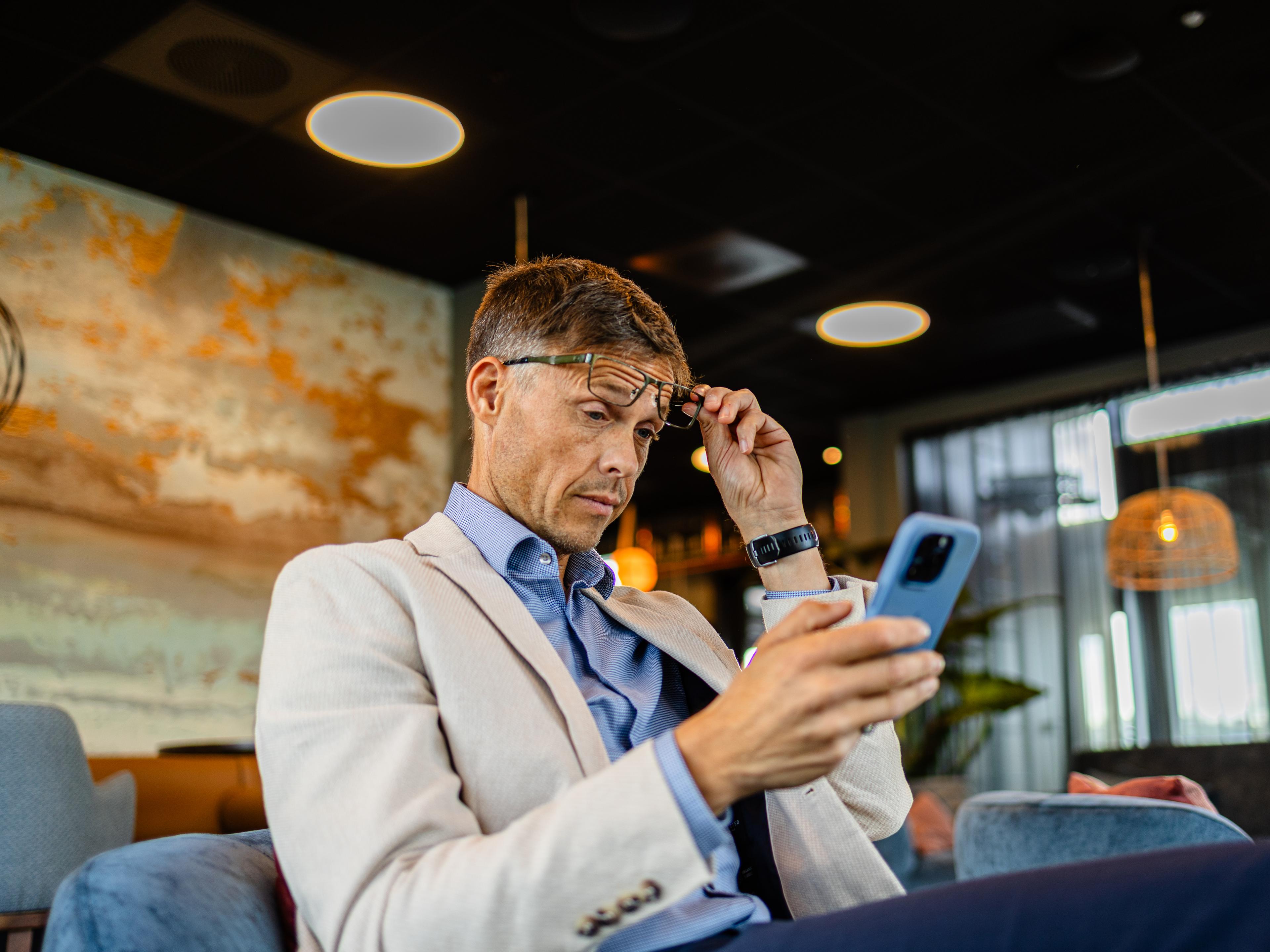 Mann løfter lesebrillene for å se på mobilen