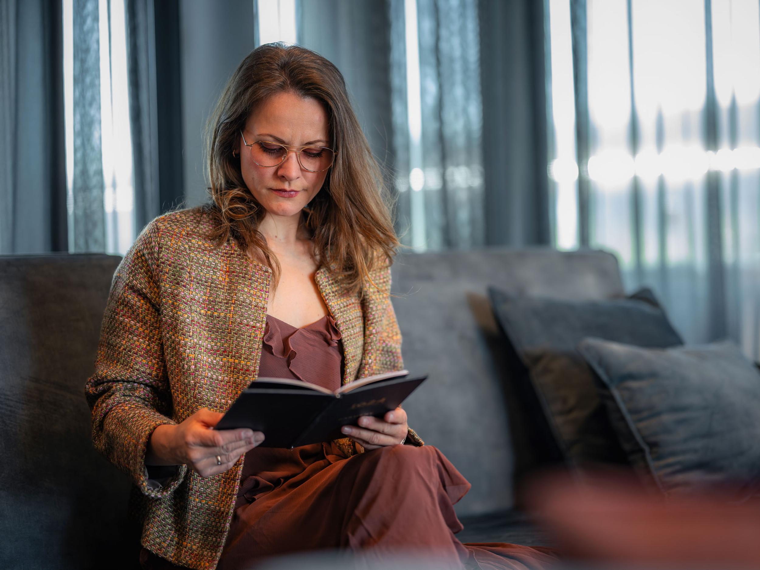 Kvinne med briller leser i sofaen