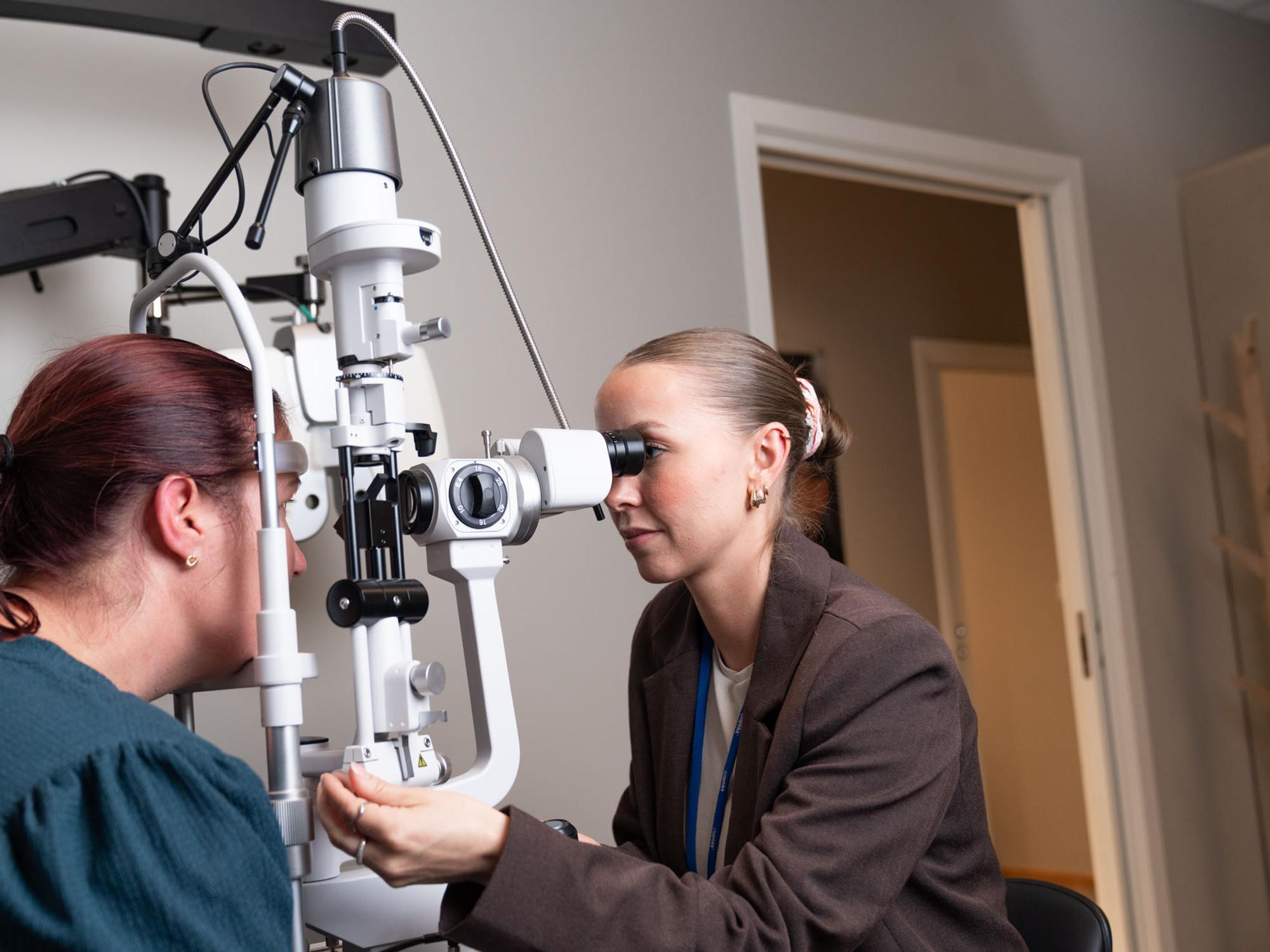 Optiker undersøker en kunde med spaltelampe i undersøkelsesrommet hos c)optikk Revetal