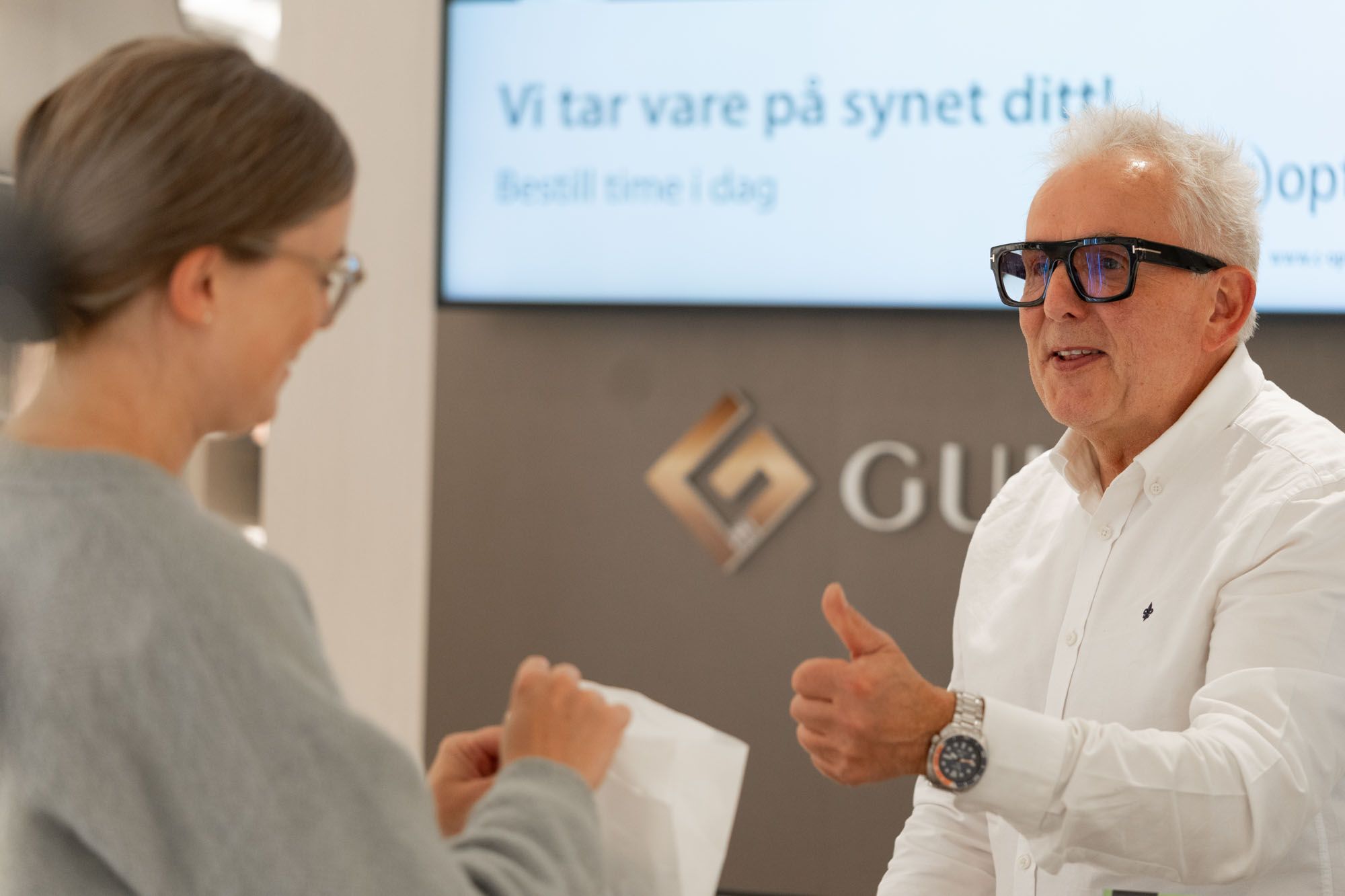 Fornøyd kunde får brillene sine ved skranken hos c)optikk Revetal