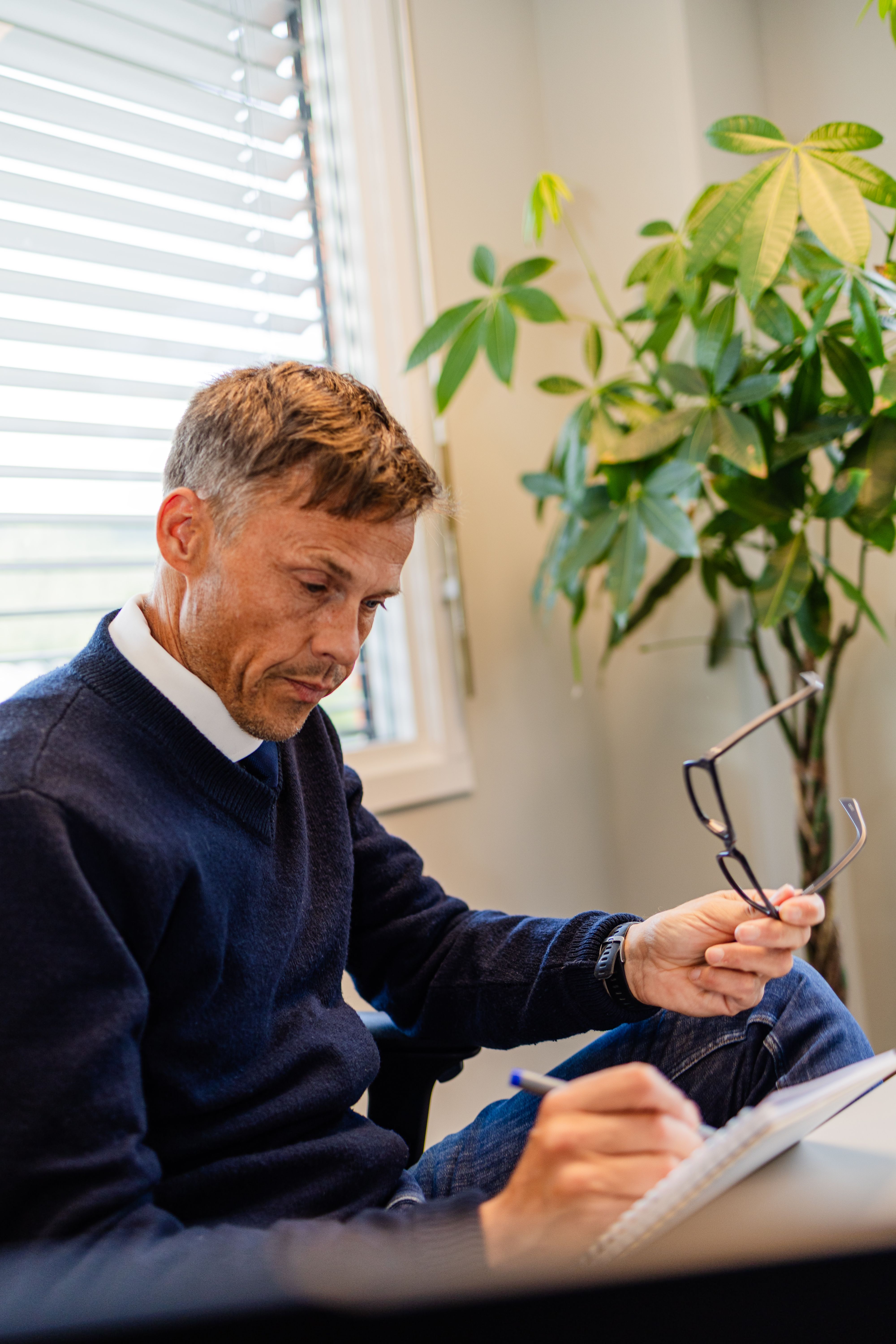 Mann med briller i hånden noterer ved pulten