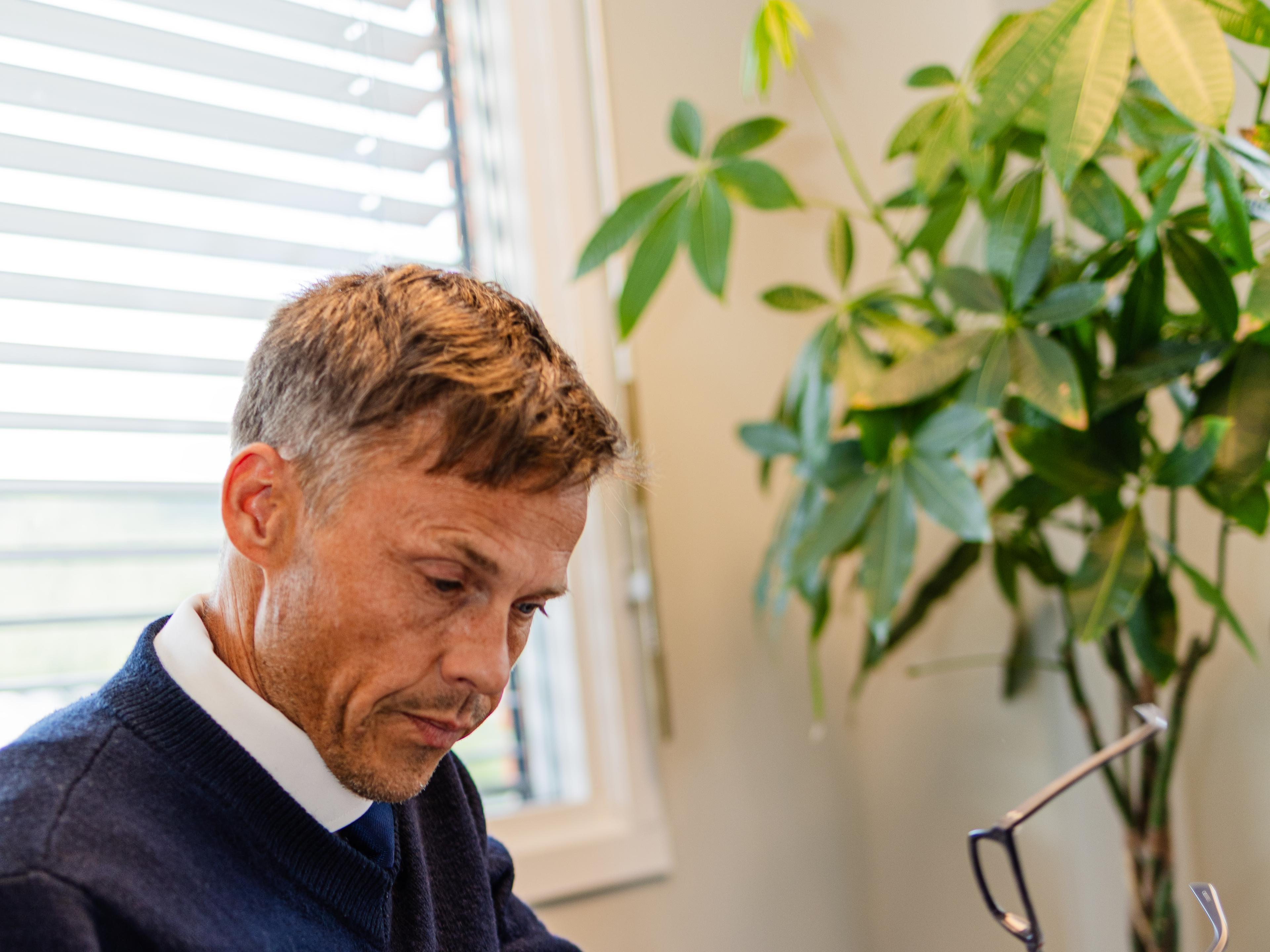 Mann med briller i hånden noterer ved pulten
