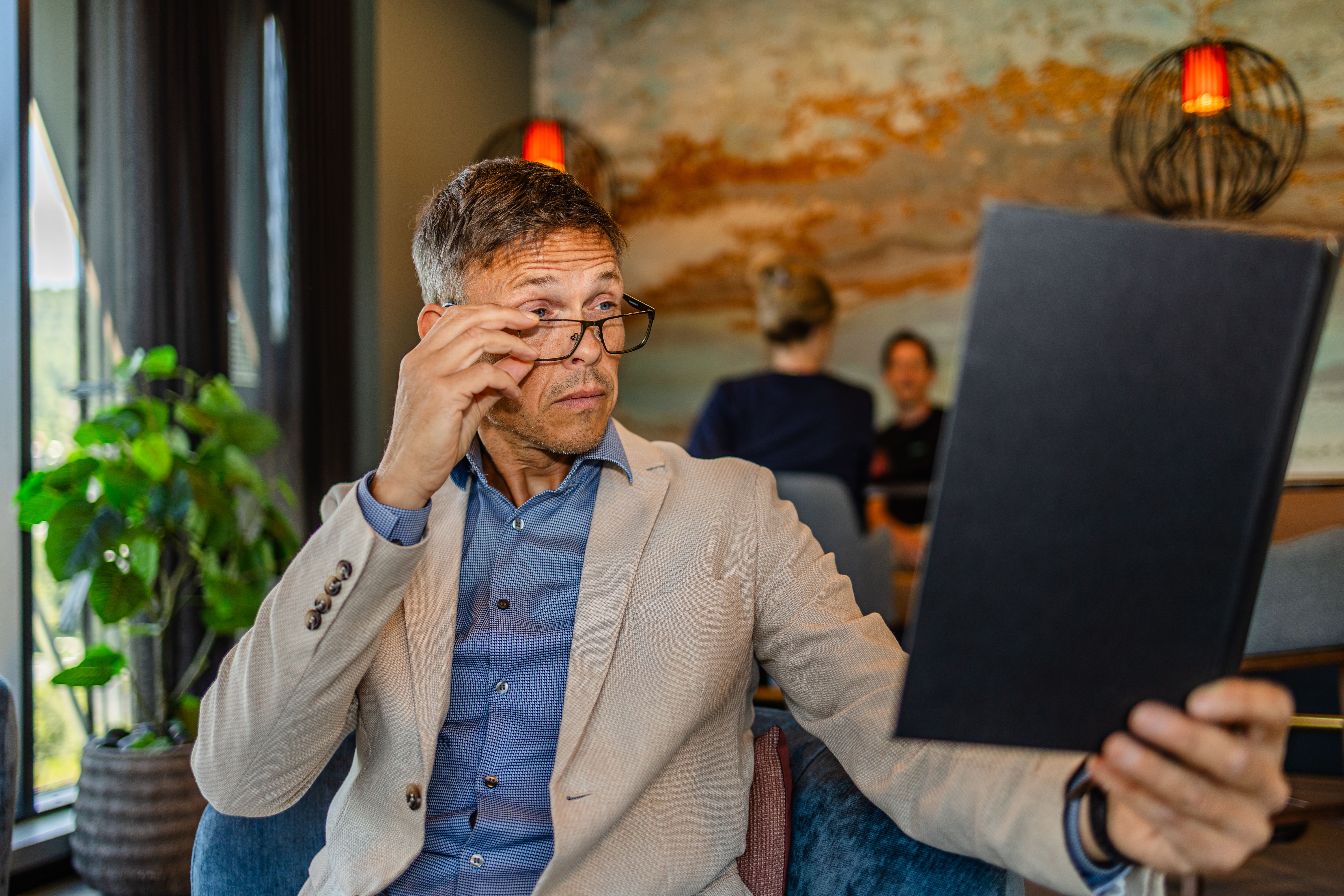 Mann kikker over brillene for å lese menyen