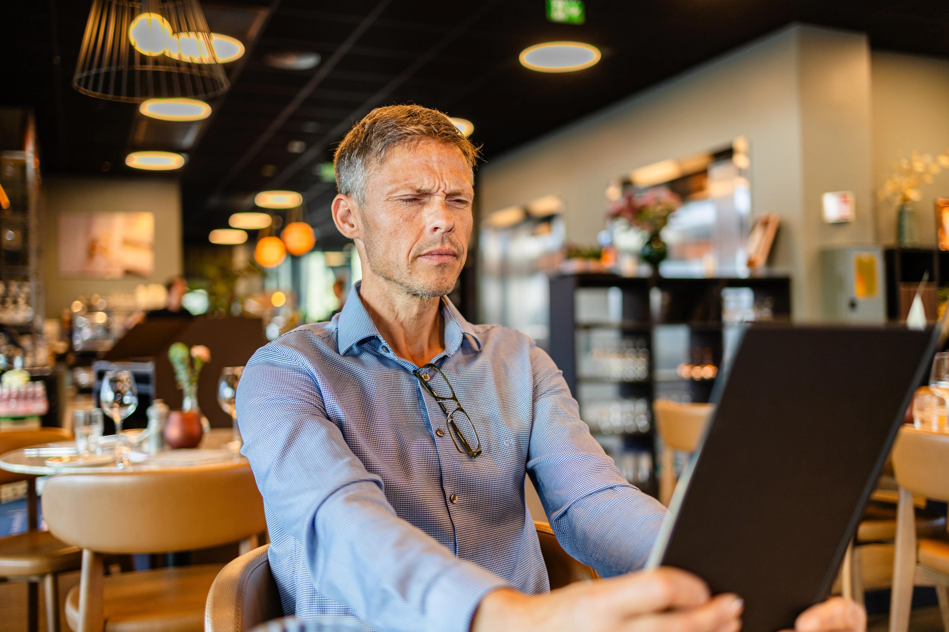 Mann myser på menyen på strak arm — et klassisk tegn på presbyopi