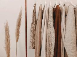 Neutral colored tops hanging from white hangers against beige background.