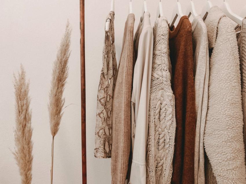 Neutral colored tops hanging from white hangers against beige background.
