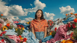 A woman standing in the center of a pile of clothes, grappling between the ideal sustainable lifestyle.