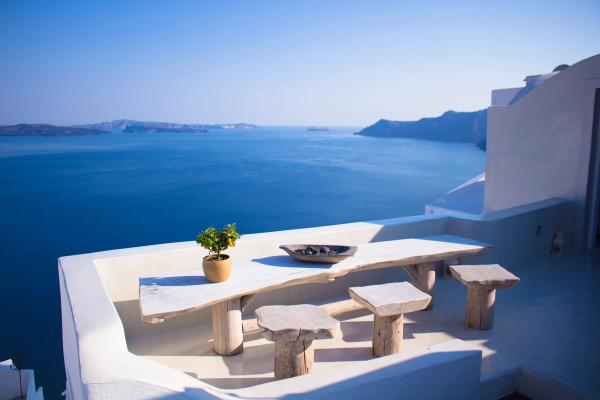 White table and wooden chairs on a white balcony over the blue sea.