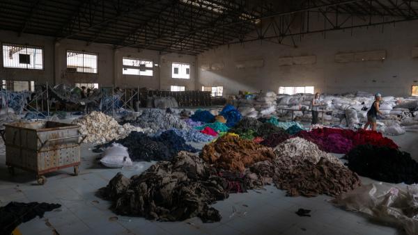 Piles of dyed fabrics on the ground of an old, dark factory.