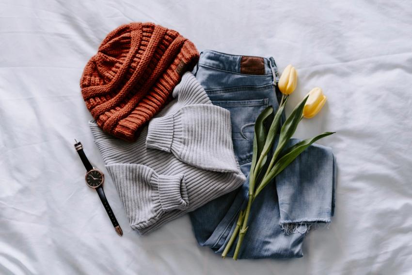 Casual outfit folded and laid out on bed sheets.