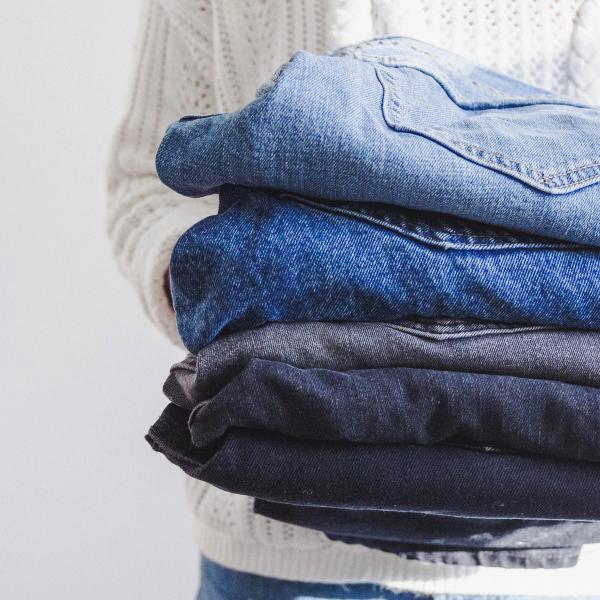 A cropped image of someone in white sweater holding five pair of men's jeans.