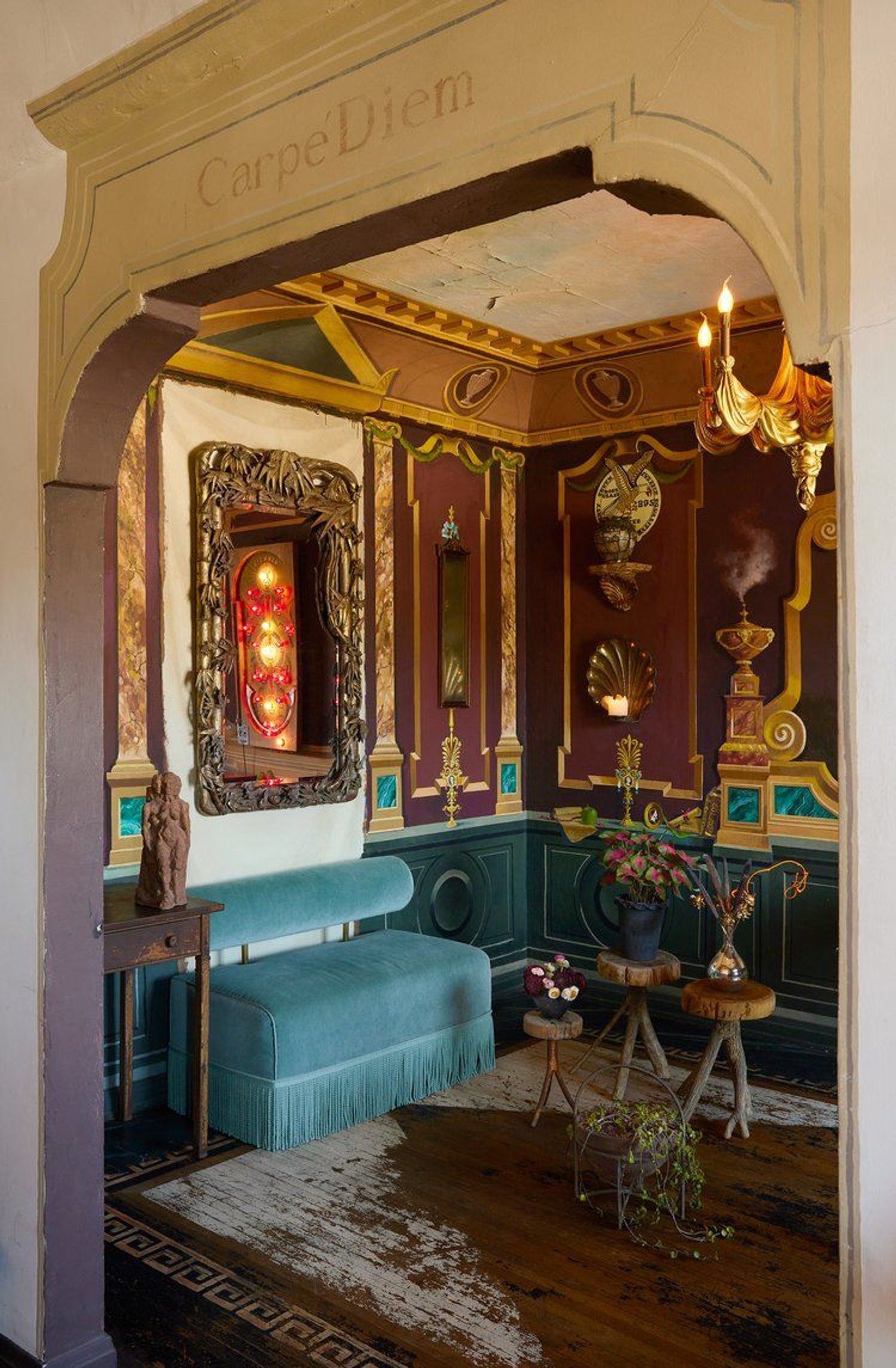 An ornate room seen through an arch marked Carpe Diem, with a blue velvet bench in it.