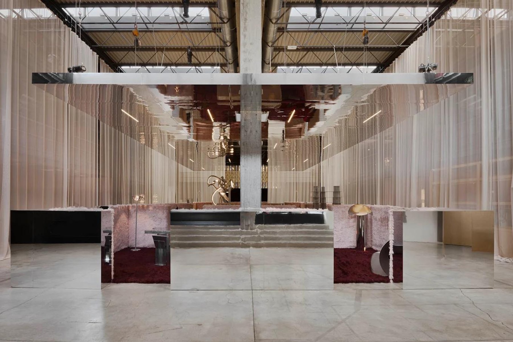 A pavilion of pink hanging curtains in a concrete hall, with two glossy red tables under a steel frame.