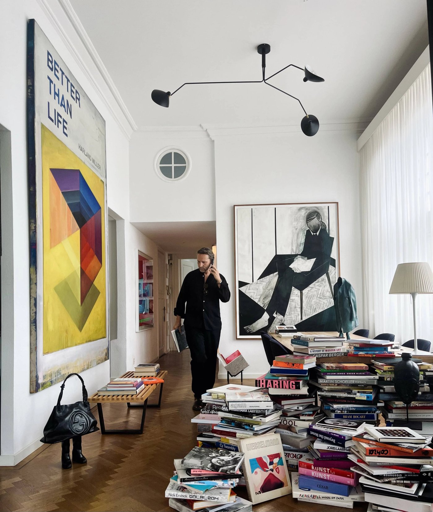 A tall apartment hung with large artworks, with stacks of art books across the floor.