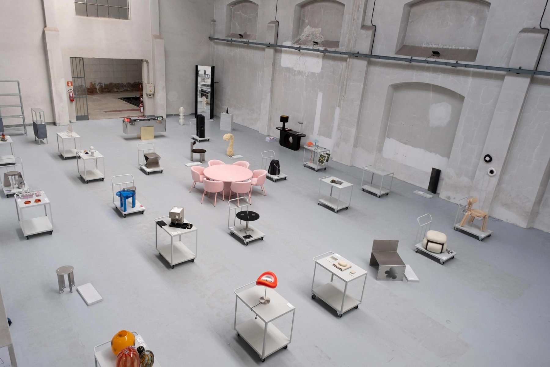 An exhibition hall with objects on glass plinths and a pink table at its centre.