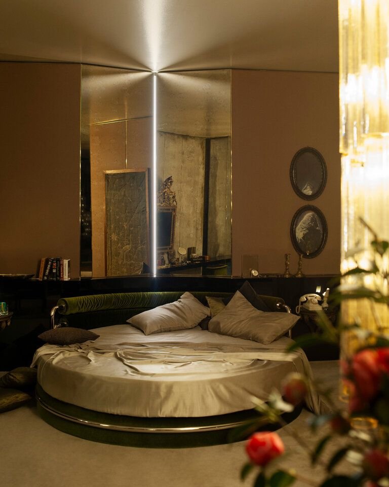 A round bed in a brown bedroom, with mirrored walls behind it.