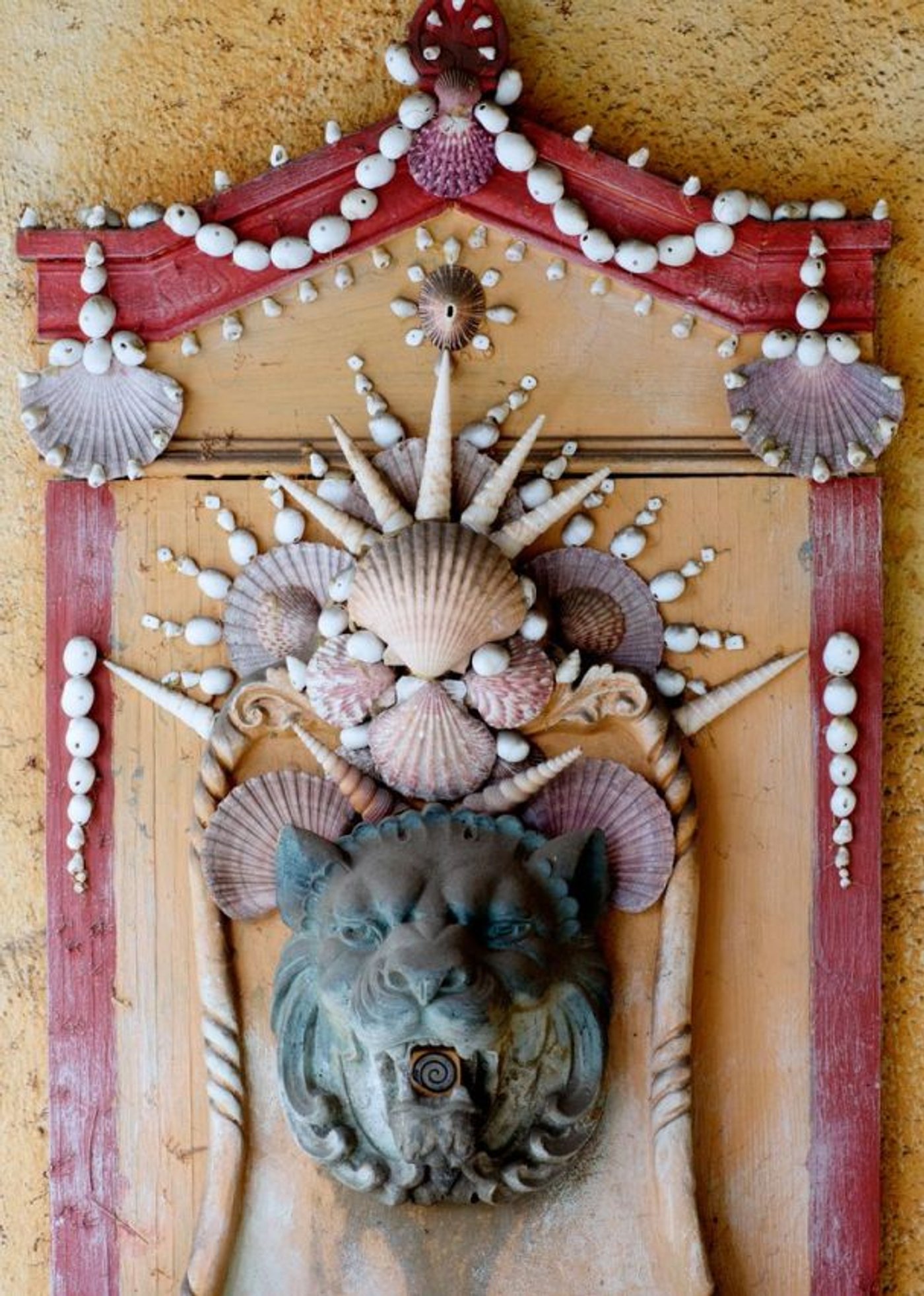 A wall fountain decorated with shells around a stone lion head.