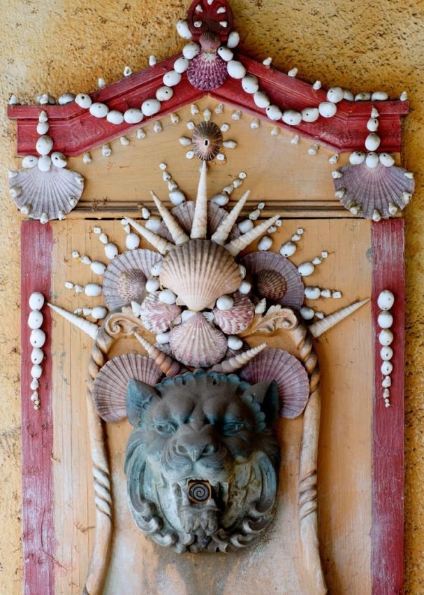 A wall fountain decorated with shells around a stone lion head.