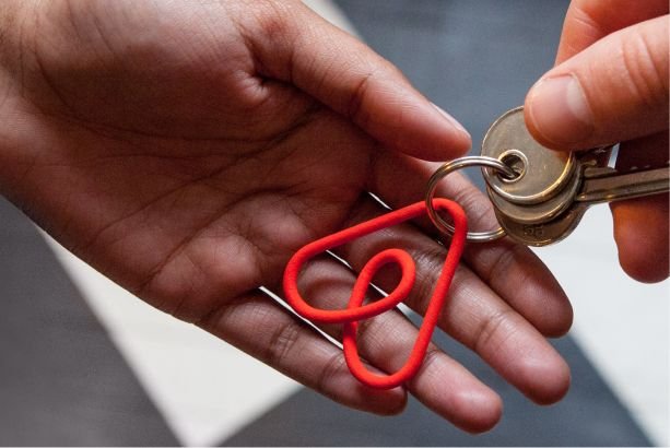 A hand passing keys with a red Airbnb keyring on them.