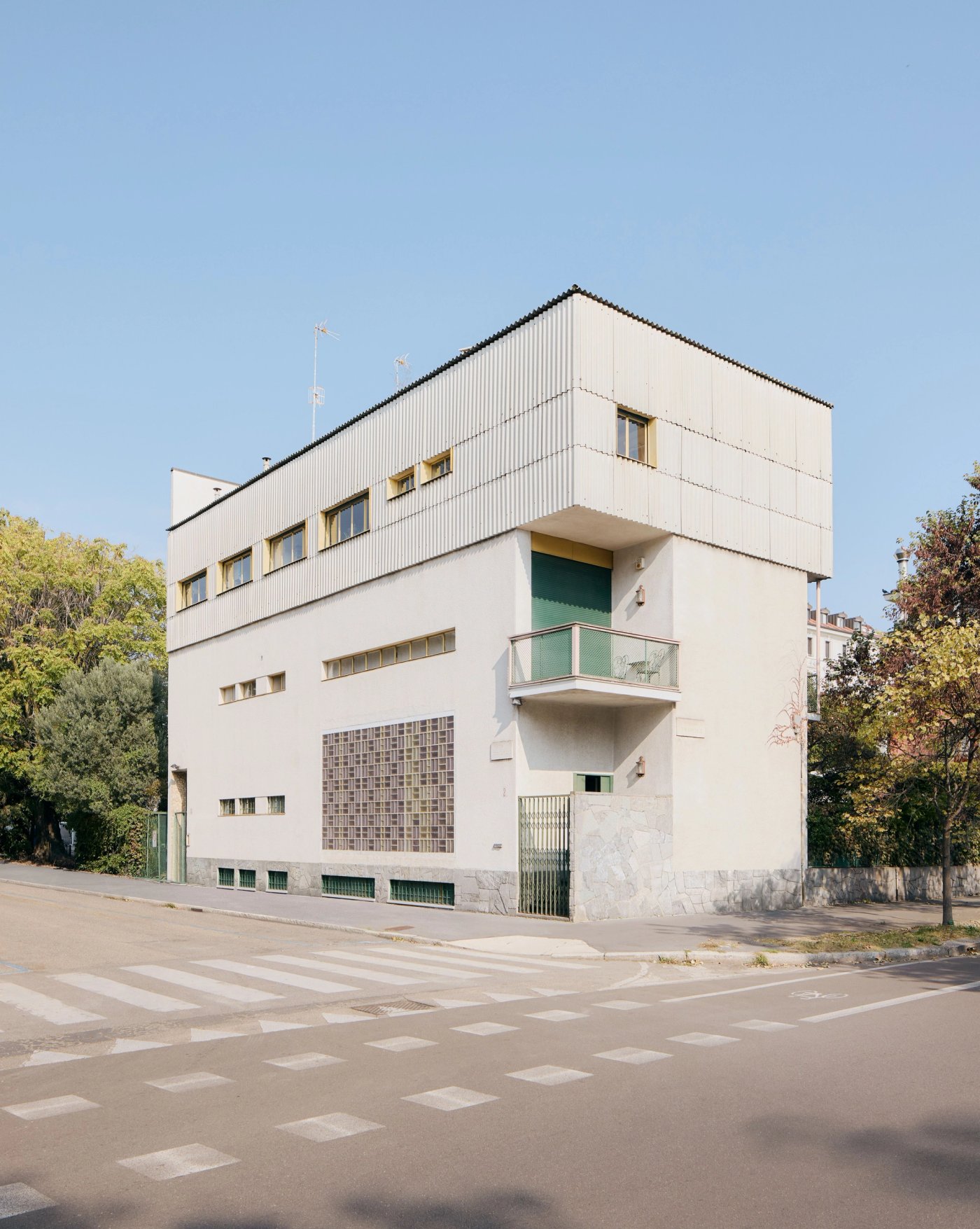 A white modernist villa on a Milan street corner, with a glass block window and a first floor balcony.