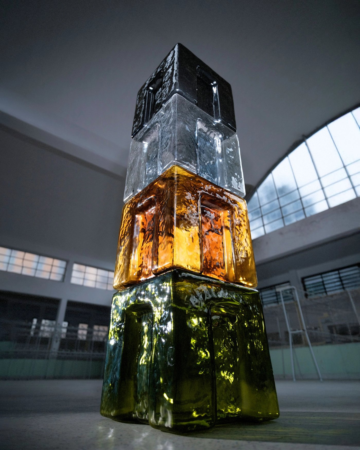 A stacked sculpture of cast glass blocks, amber and green, lit from within in a vaulted hall.