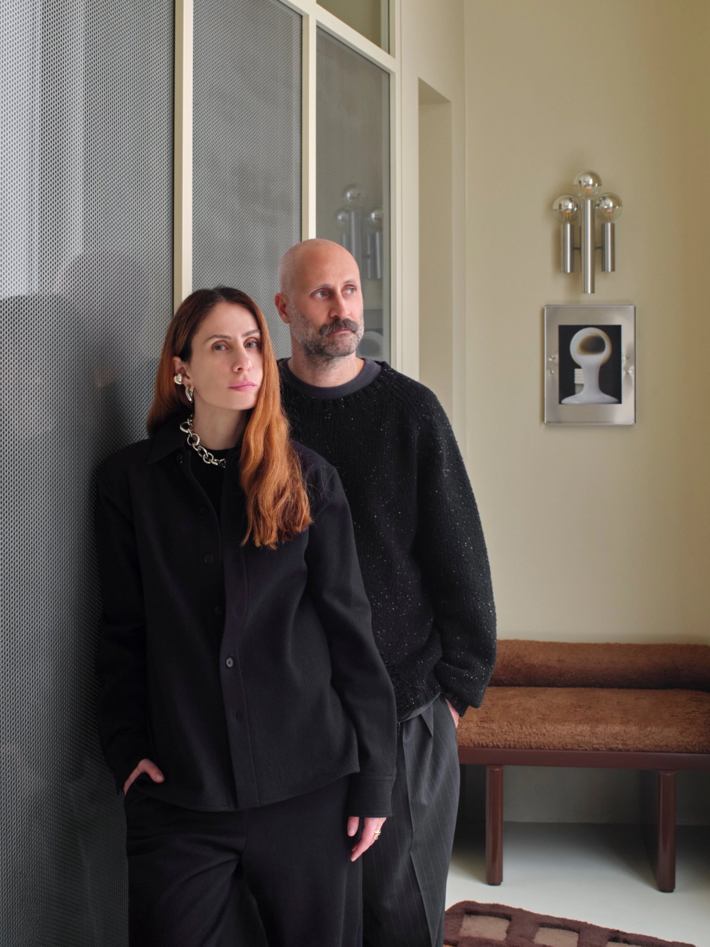 A designer couple in black stand together in their apartment.