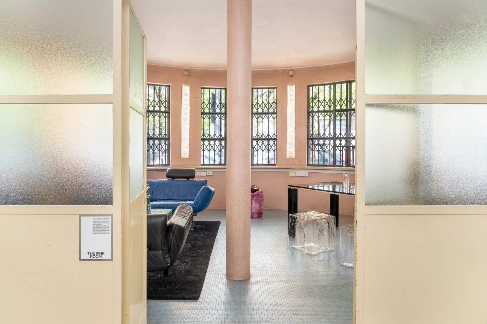 A pink room seen through glass doors, with a blue sofa and a barred window behind it.